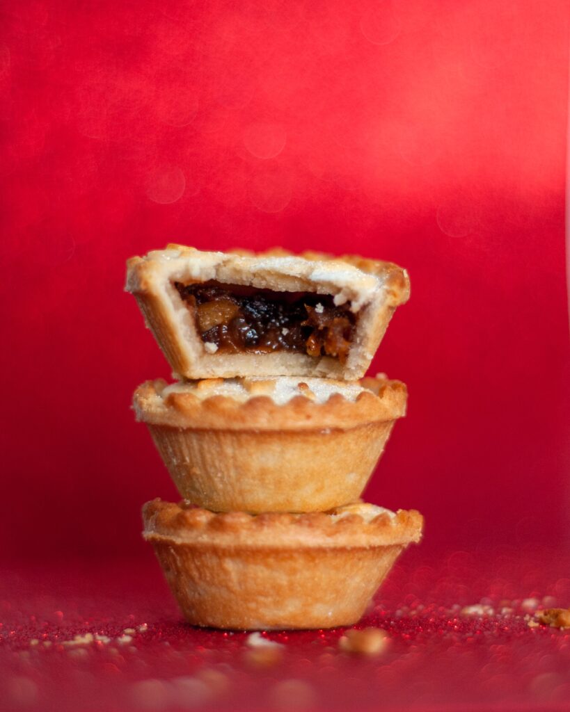 Red background with a stack of three mince pies on top of each other. One is cut open to see the filling inside. Photo credit: Marina Hannah on Unsplash.